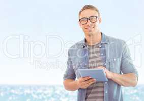 Man with tablet against blurry water on sunny day
