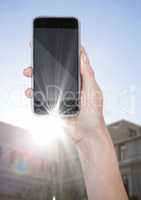 Hand with phone against blurry building with flare