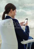 Businesswoman sitting on chair with smart phone against sky