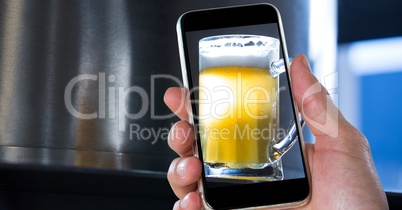 Hand taking picture of beer glass through smart phone at bar
