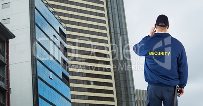 Rear view of security guard talking on bluetooth device while standing against buildings