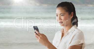 Woman looking at phone against blurry beach and flare