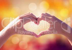 Hands making heart shape with sparkling light bokeh background