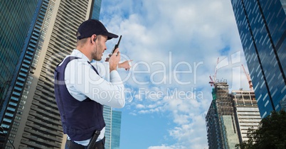 Security guard talking on walkie talkie and gesturing while standing by buildings against sky