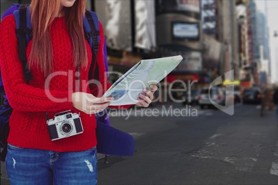 Woman traveler carrying bag is looking at map against cityscape background