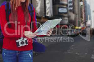 Woman traveler carrying bag is looking at map against cityscape background