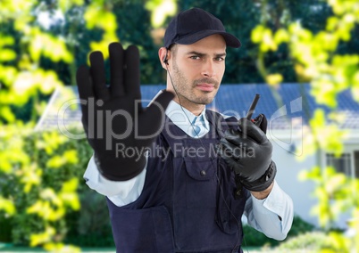 Security guard with hat, headphone and walkie-talkie, saying stop with his hand in front of the hous