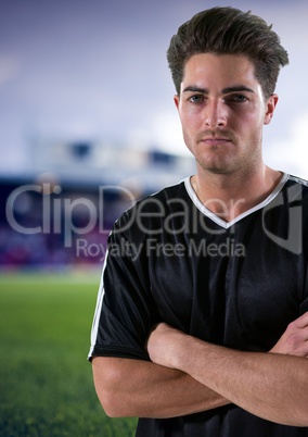 serious soccer player with hand folded and black t-shirt, field blurred background