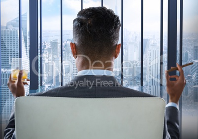 Back of seated business man smoking cigar and drinking while looking at blue window