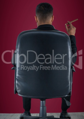 Back of seated business man smoking cigar against maroon background
