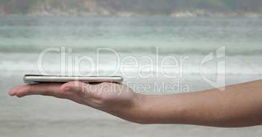 Hand with phone on palm against blurry beach