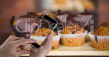 Hand photographing muffins through smart phone at bakery