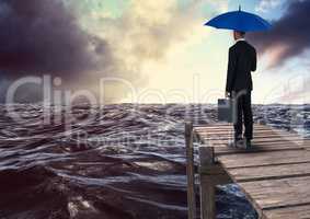 Rear view of businessman holding blue umbrella with briefcase and looking st sea while standing on p