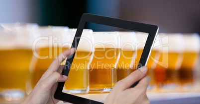 Hands photographing beer glasses through digital tablet at bar