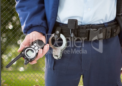security guard with walkie-talkie on his hand and cuffs on the belt in front of the fence