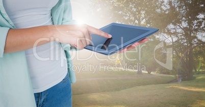 Woman mid section with tablet against blurry park with flares