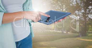 Woman mid section with tablet against blurry park with flares