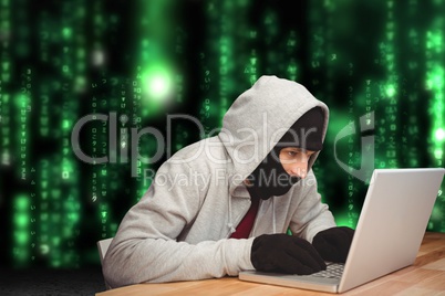 Cyber criminal hacking from a laptop on a desk against matrix code rain background