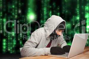 Cyber criminal hacking from a laptop on a desk against matrix code rain background