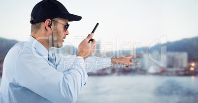Security guard with walkie talkie pointing against blurry skyline