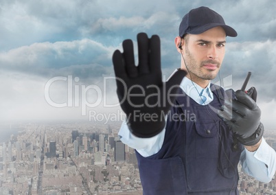 Security guard with walkie talkie and hand up against skyline and clouds