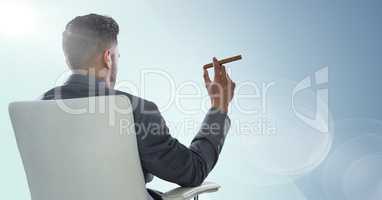 Back of seated business man smoking cigar against blue background and flare