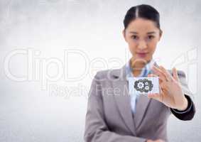 Business woman holding out card showing grey cloud and gear graphic against white wall
