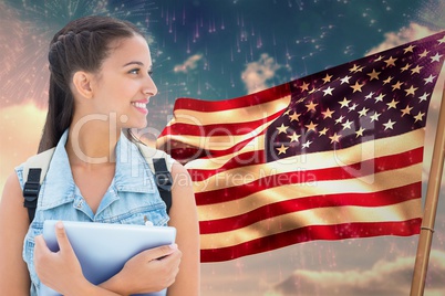 student carrying a bag is holding a tablet computer against american flag