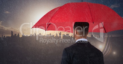 Back of business man with umbrella against skyline with sunset and rain