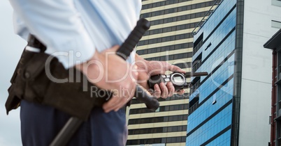 Mid section of security guard holding baton and walkie talkie standing against buildings