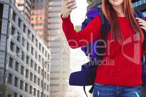 A woman traveler wearing a bag is taking a picture with her smartphone against building background
