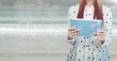 Woman mid section with polka dot top and tablet against blurry beach