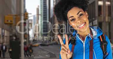Smiling hipster carrying backpack with camera gesturing peace sign standing in city