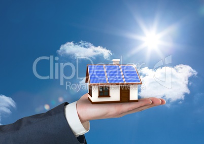 Digital composite image of cropped hand holding house with roof of solar panel against sky