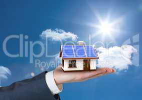 Digital composite image of cropped hand holding house with roof of solar panel against sky