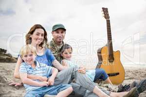 family sitting on sand with a guitar against beach background