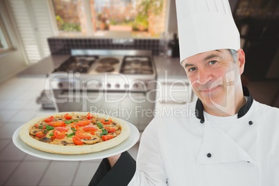 A cook wearing a chef's hat is holding a pizza on a plate against kitchen background