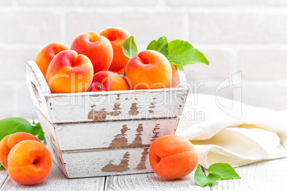 Fresh apricots with leaves on white wooden background