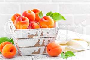 Fresh apricots with leaves on white wooden background