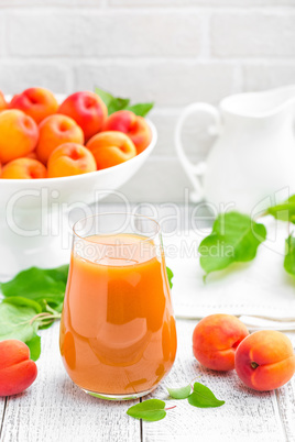 Apricot juice and fresh fruits with leaves on white wooden table