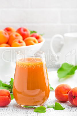 Apricot juice and fresh fruits with leaves on white wooden table