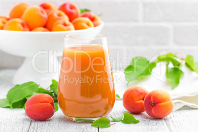 Apricot juice and fresh fruits with leaves on white wooden table