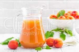 Apricot juice and fresh fruits with leaves on white wooden table