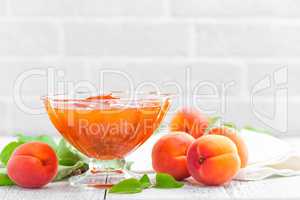 Apricot jam and fresh fruits with leaves on white wooden table