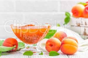 Apricot jam and fresh fruits with leaves on white wooden table