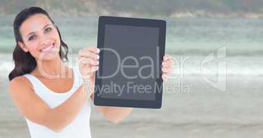Smiling woman holding out tablet against blurry beach