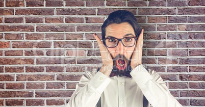 Creative businessman looking surprised while standing against brick wall