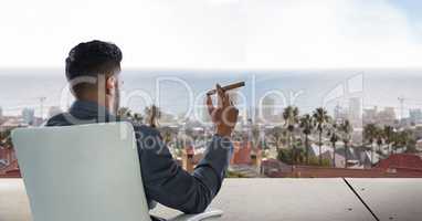 Businessman sitting on chair and looking at city while smoking cigar