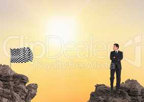 Businessman looking at checkered flag while standing on rocks against sky