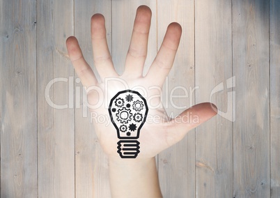 Hand with cogs in lightbulb graphic and flare in palm against grey wood panel